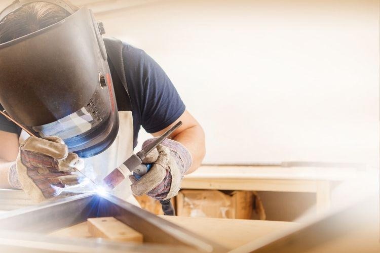 Male in face mask welds with argon-arc welding